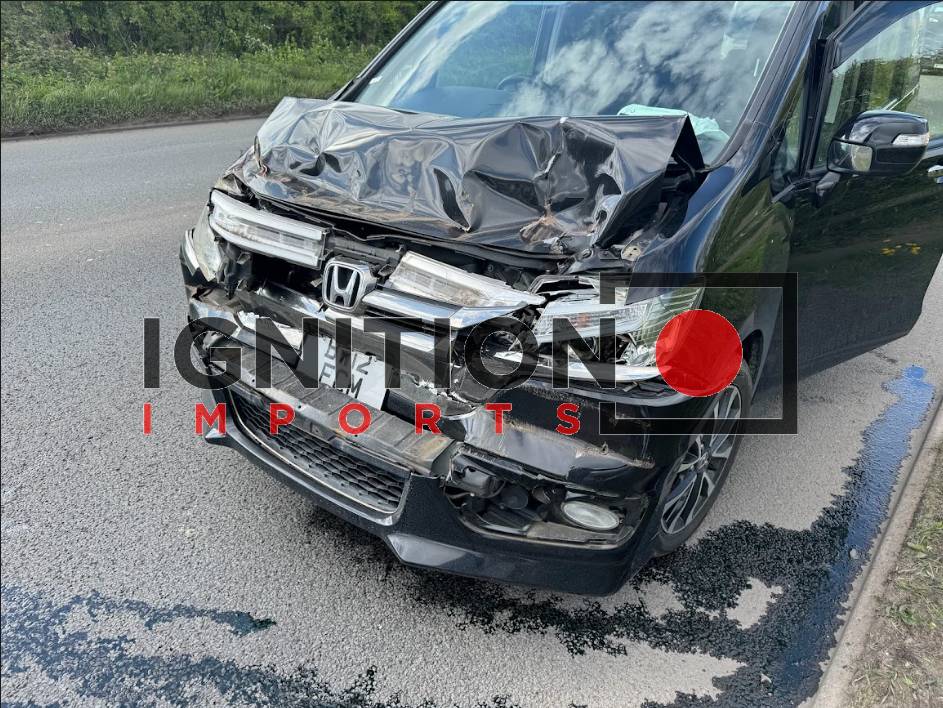 A Honda Stepwagon at the side of a road which has been in a front end crash with fluid leaking out.